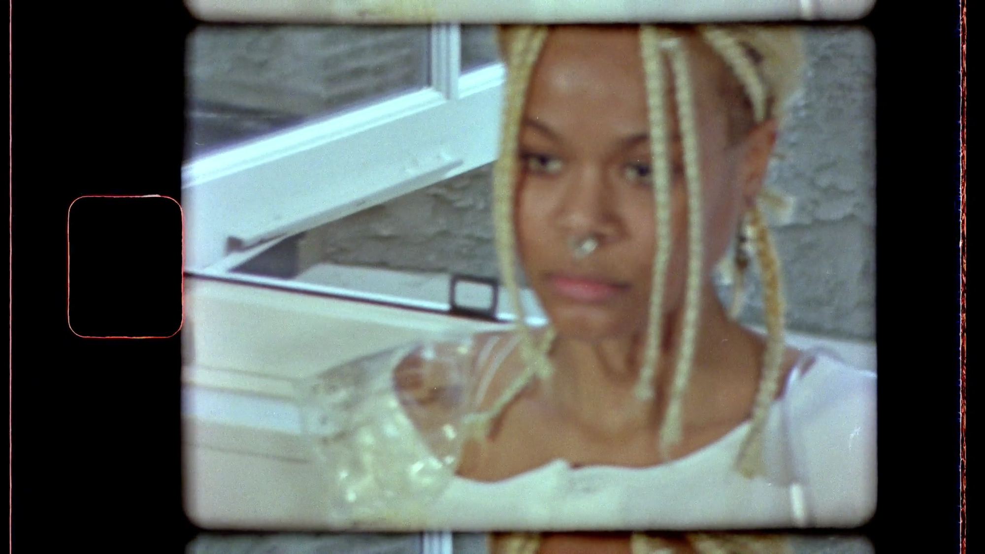 8mm frame film still of a person with blonde dreadlocks in white dress in front of a window