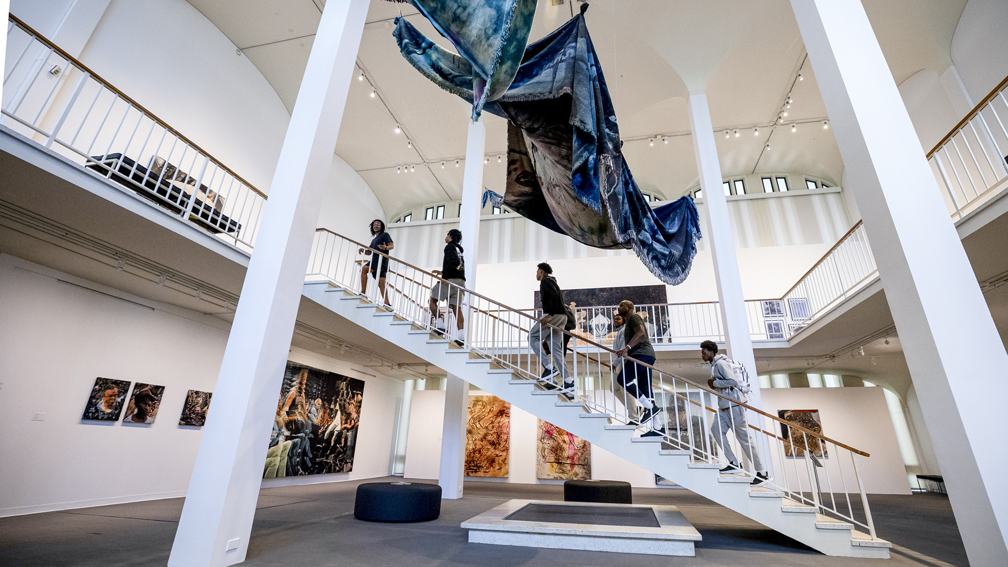 UAlbany Men’s Basketball players and coach walk up the large staircase to the second floor of the University Art Museum with exhibiting artist Noel W Anderson.  