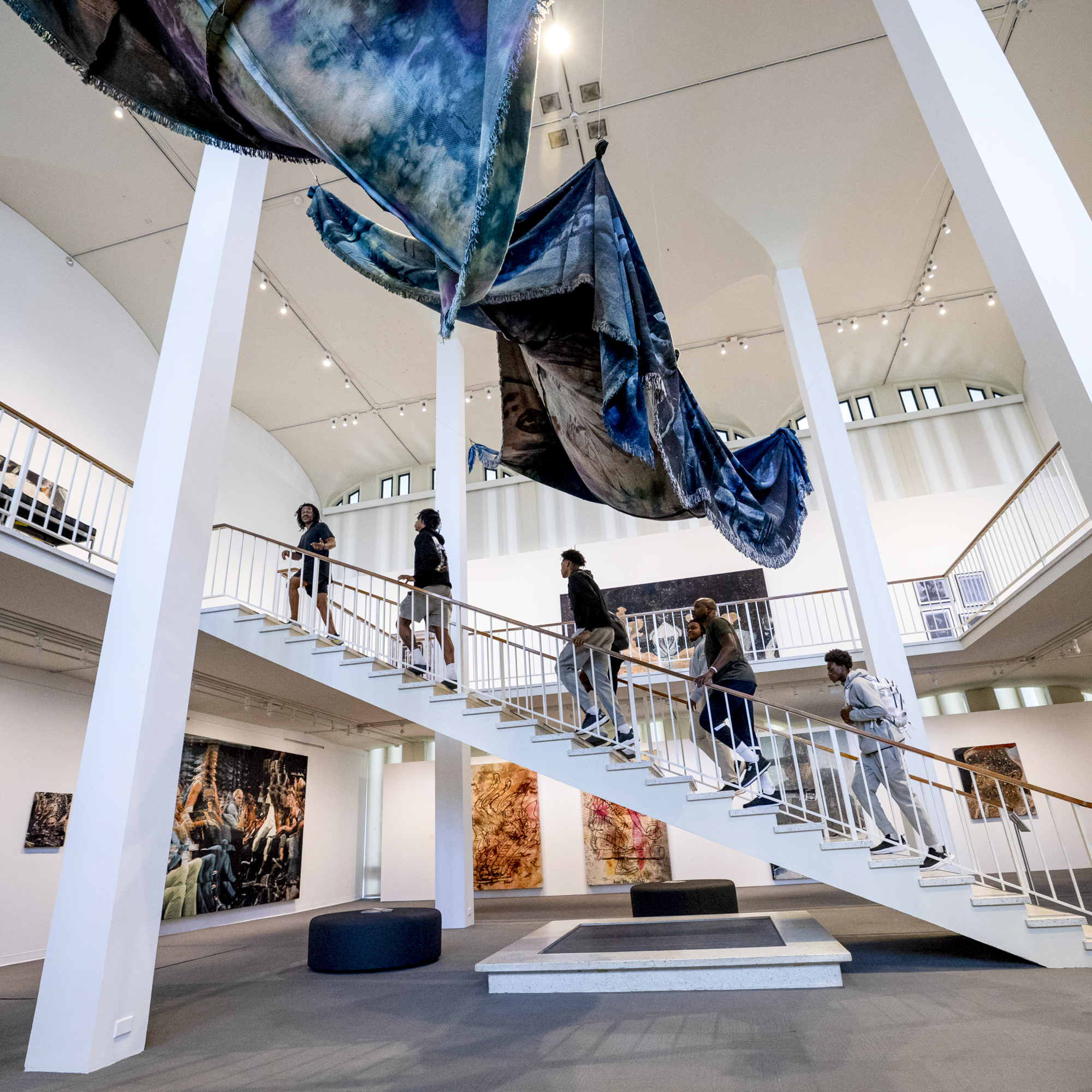 UAlbany Men’s Basketball players and coach walk up the large staircase to the second floor of the University Art Museum with exhibiting artist Noel W Anderson.  