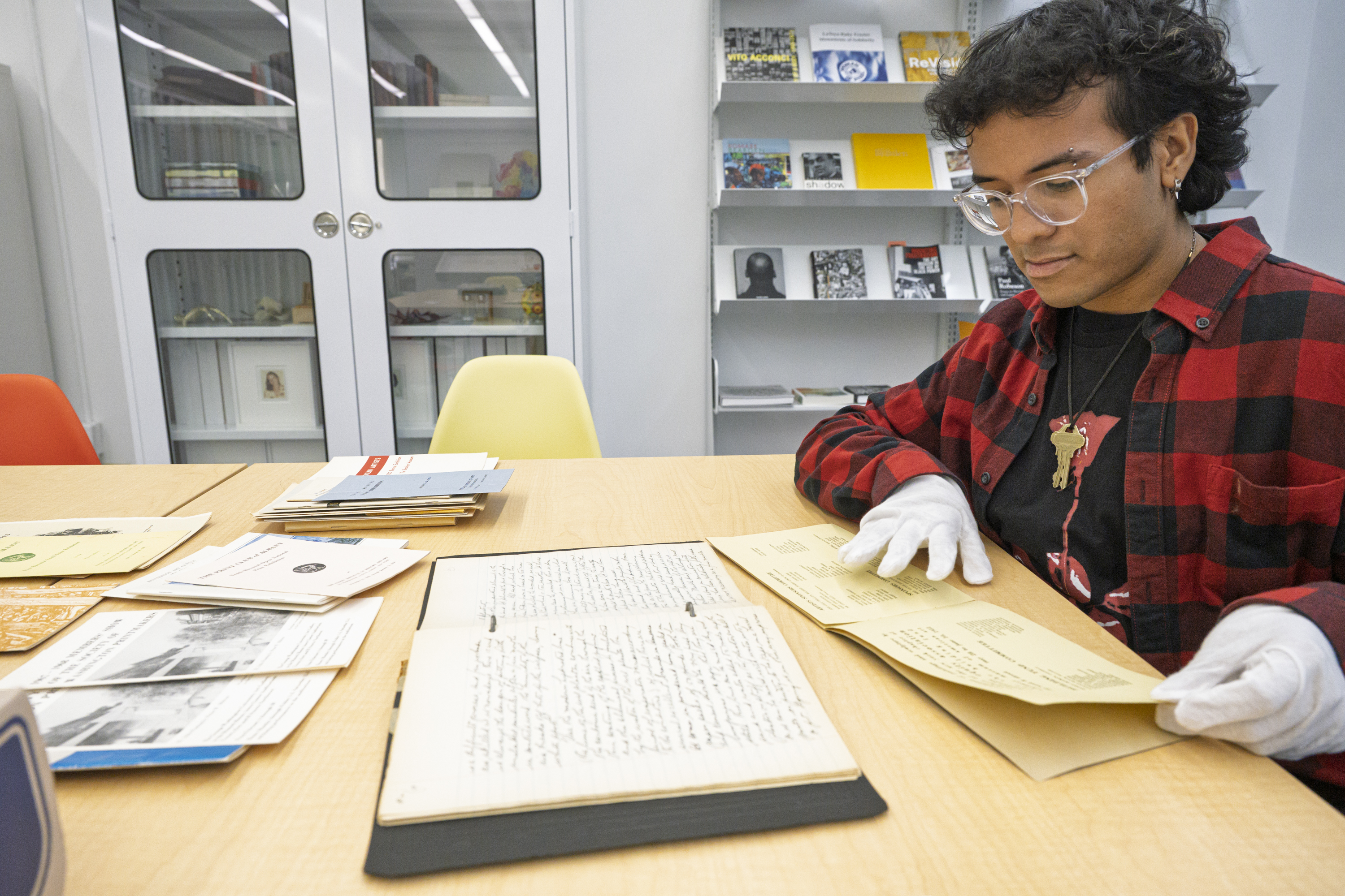 Collections Intern Diego Herrera ’26 sits at a table in the Collections Study Space with white gloves on, reading notebooks and correspondence of the artist Hilda Katz, an artist whose work is included in the Collections.