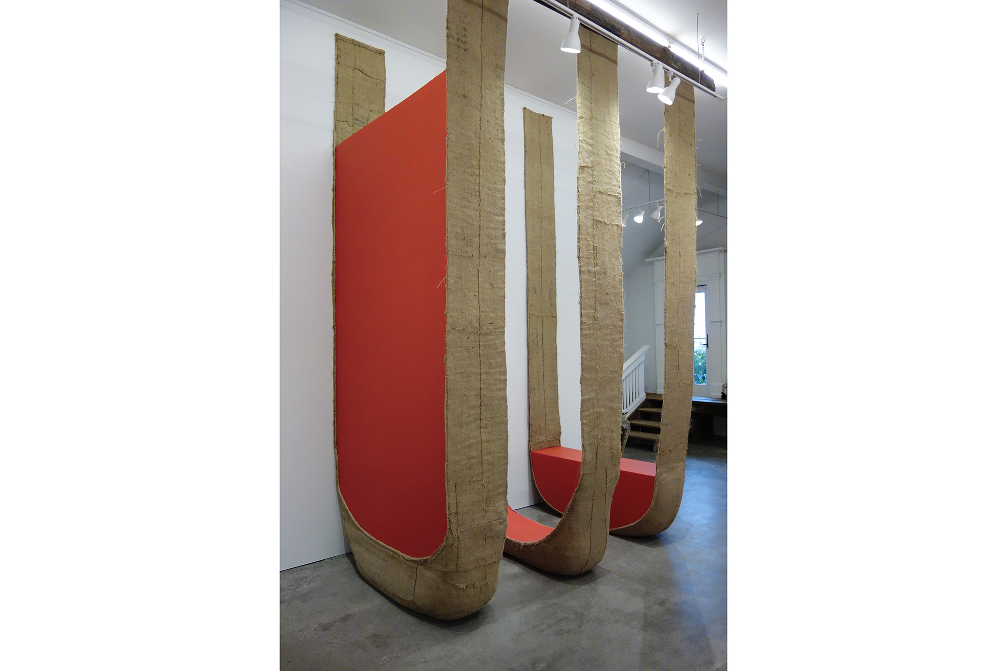 Three large “U” shaped sculptures with bright red interiors by upcoming exhibiting artist Howard Schwartzberg sit perpendicular to a white gallery wall. 